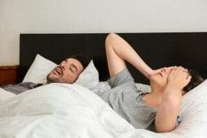 Tiredness and restlessness of a sleeping woman on bed with a man due to Brain Fog