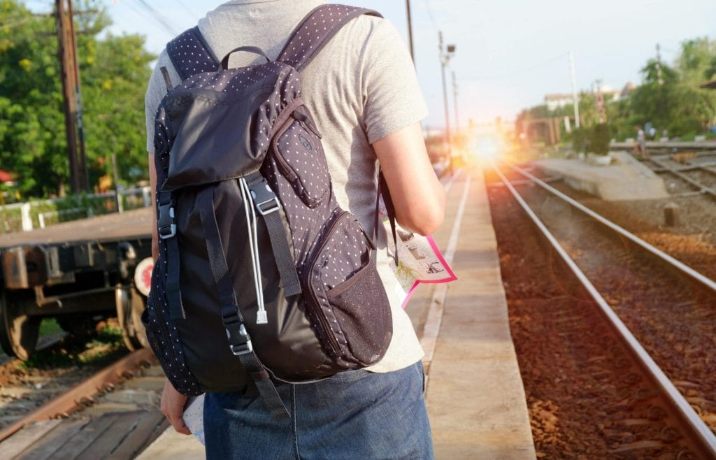 A person with a backpack waits at a railway station during daytime.