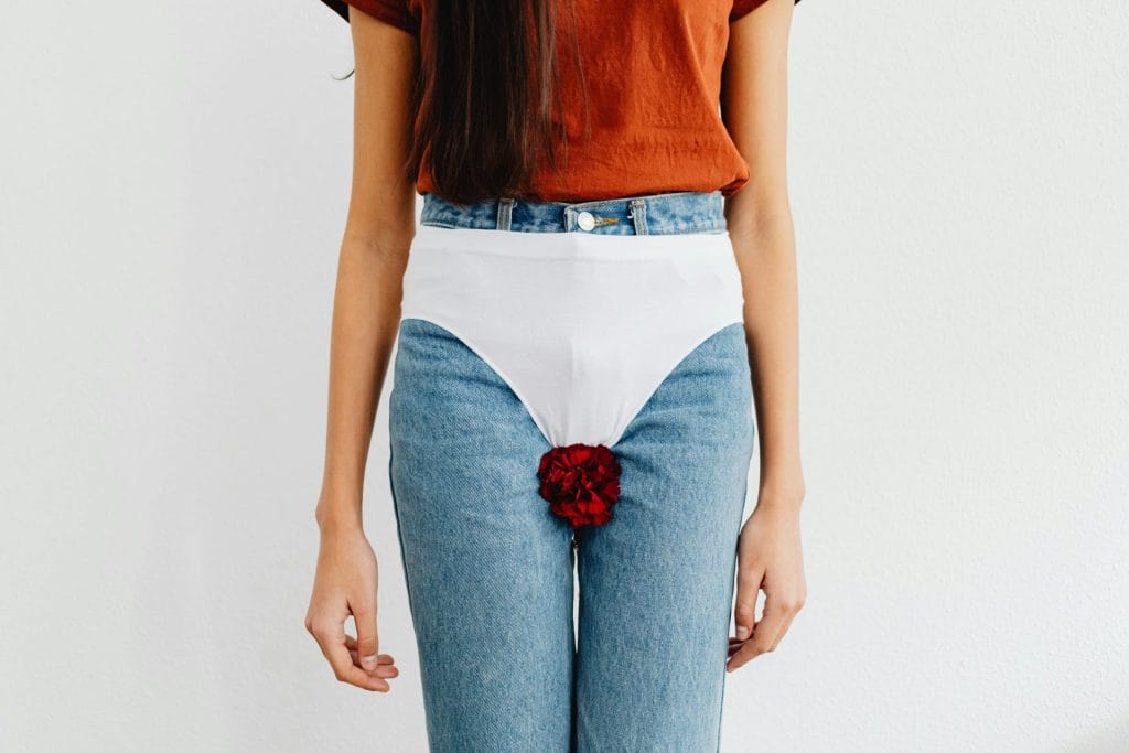 Symbolic representation of menstruation using red flower on jeans, addressing social issues.