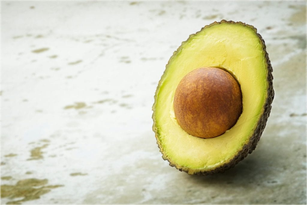 Close-up of a ripe avocado half with seed, showcasing its vibrant green flesh on a soft textured background.