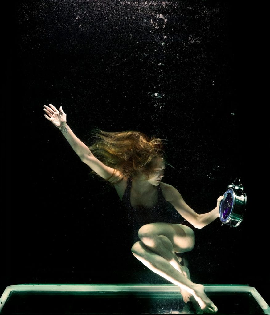 Artistic photo of a woman underwater holding a clock, symbolizing time.
