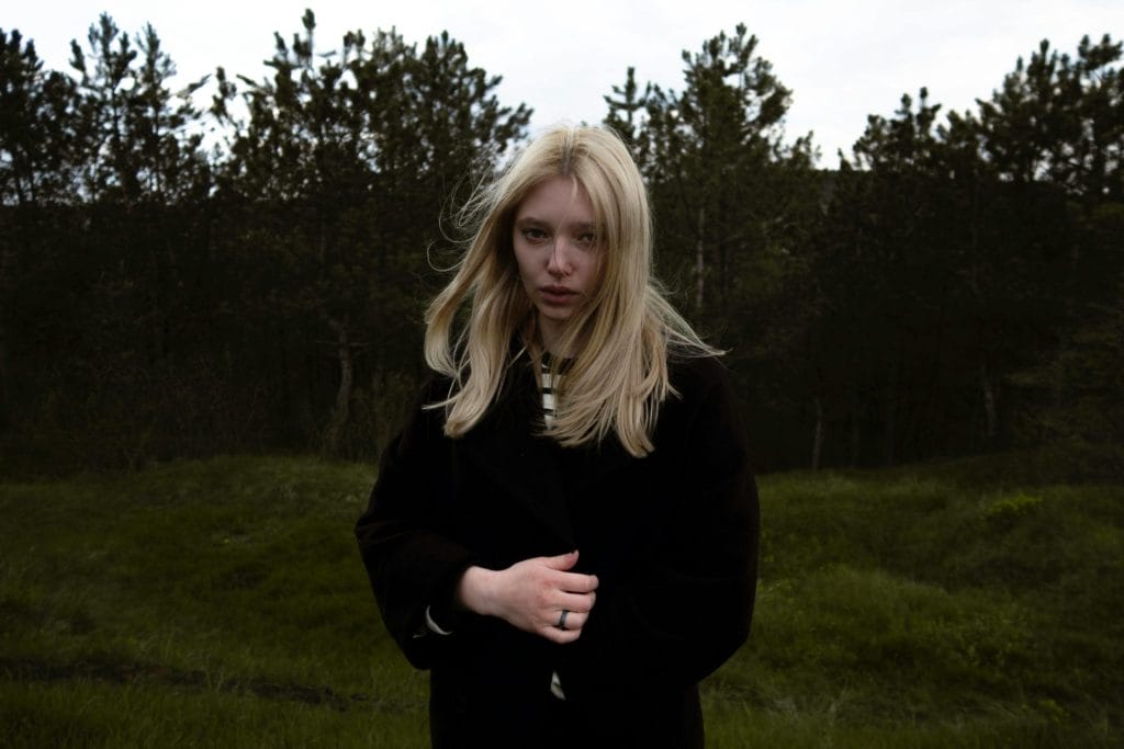 Portrait of a young woman with blonde hair in a black coat outside.