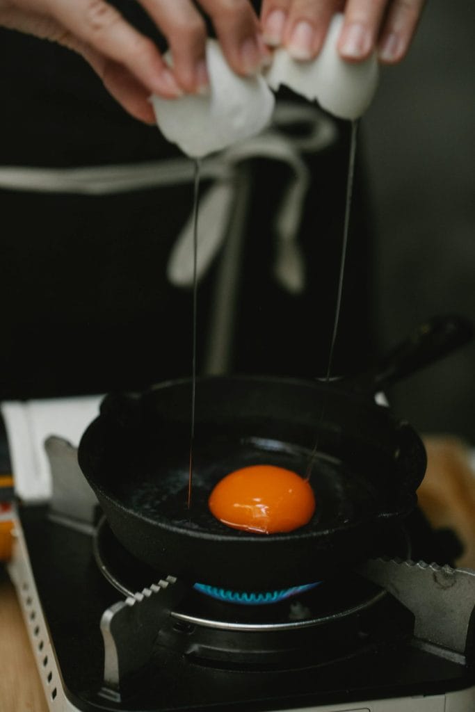 Close-up of breaking an egg into a frying pan over a stove, highlighting breakfast cooking.