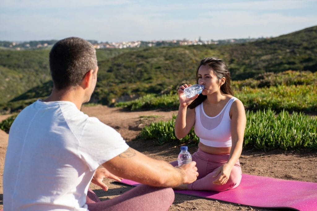 A man and woman enjoy an outdoor yoga session with water bottles in the scenic hills of Portugal.