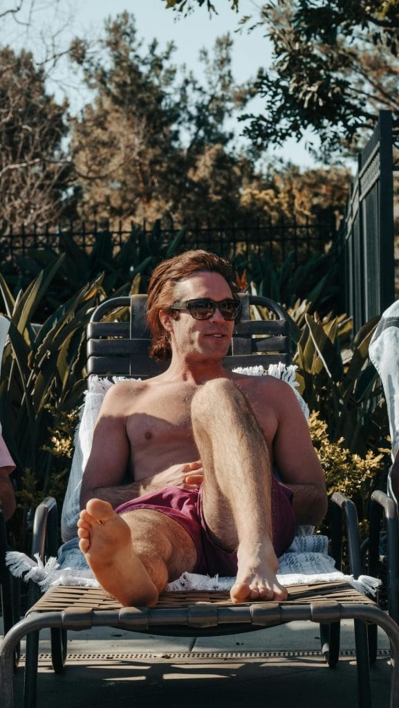 A man lounging in swimwear enjoying the sun at a resort poolside in summer.