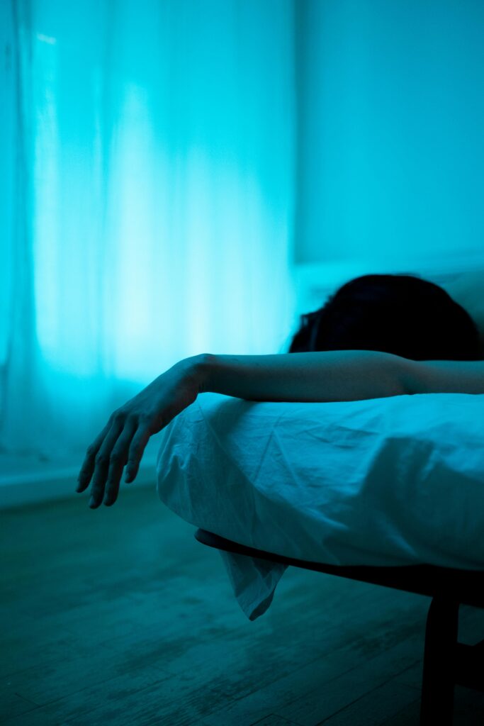 A serene and moody bedroom scene showcasing a person resting with an arm draped over the bed.