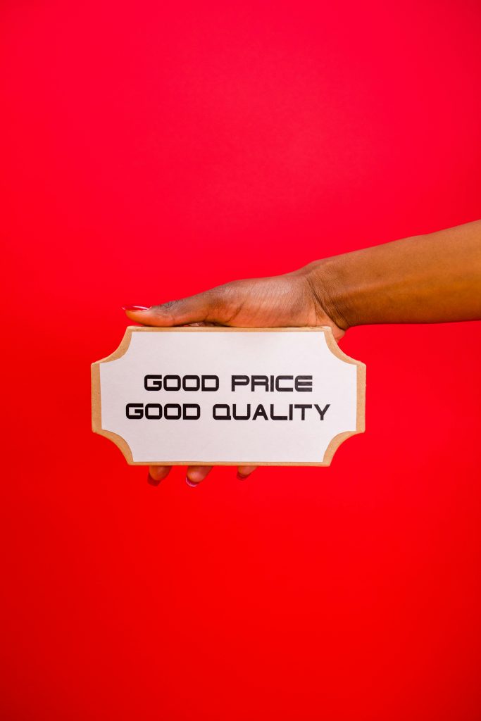 A hand holding a sign with &#039;Good Price, Good Quality&#039; text against a bright red background.