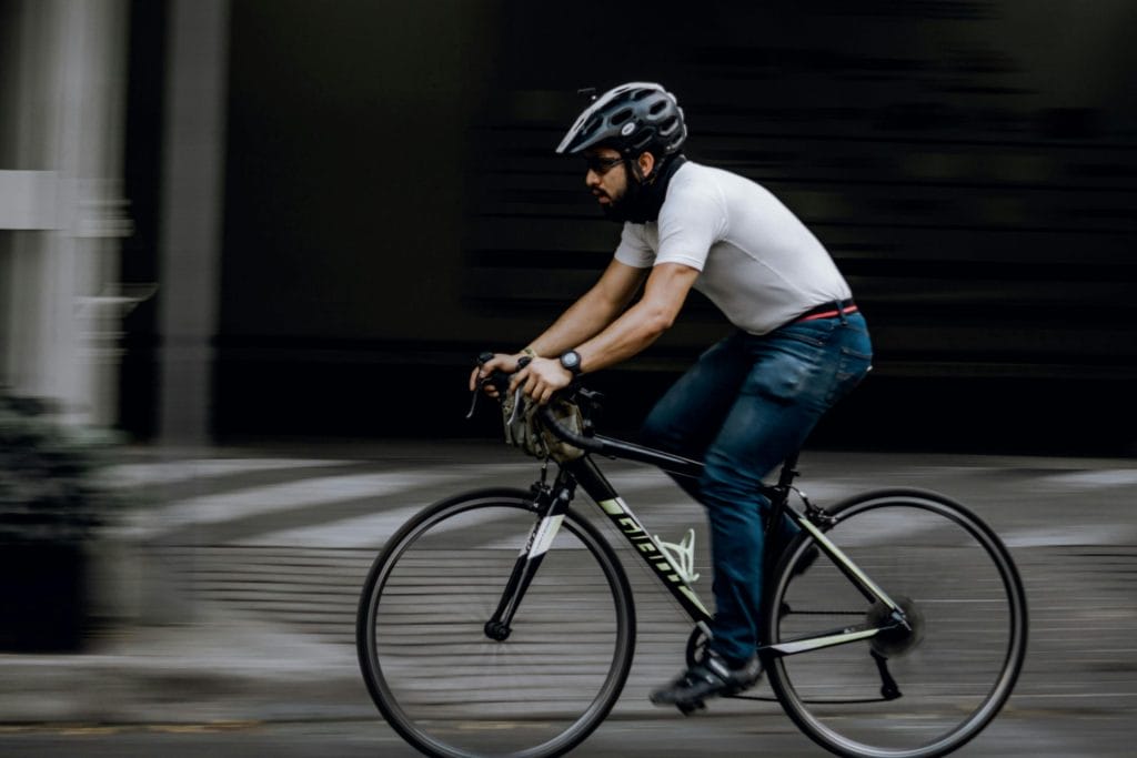 A man in casual attire riding a bicycle swiftly through a city street, showcasing motion and focus.