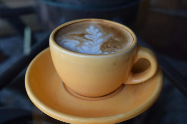 Capture of a latte with intricate art, served in a yellow cup on a table.