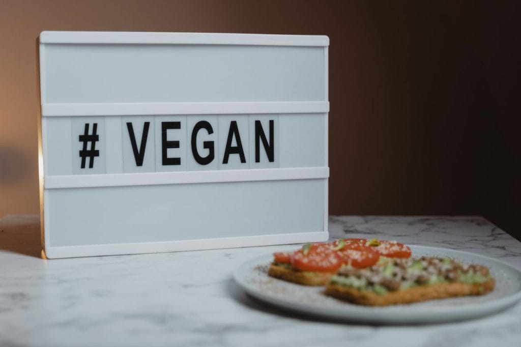 Stylish lightbox displaying '#VEGAN' beside a plate of avocado toast on a marble surface.